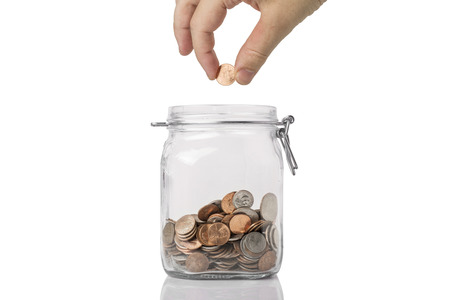 Penny Pinching or saving concept - a jar of American coins with a hand about to drop a penny into...