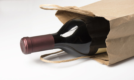 A bottle of red wine in a paper bag, perhaps being given as a gift or bought at a liquor store, on a white background with reflection and shadowの写真素材