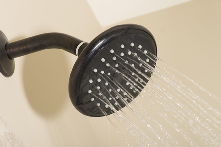 An oil-rubbed bronze Shower head on a shower wall with running waterの写真素材