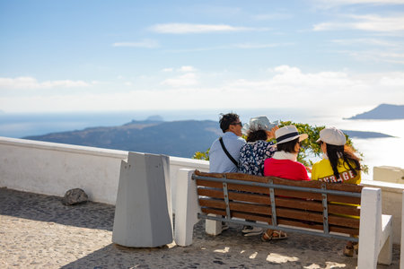 05.11.21 - Santorini, Fira, Greece: Fira capitol town of Santorini. Main square, Chinese people sitting on bench, traditional white architecture, summer day. Luxury vacayのeditorial素材