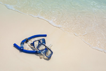 Summer beach snorkel gear, googles on soft sand with calm waves splashing. Tropical summer beach landscape, vacation or holiday concept. Relaxing view of recreational activityの写真素材