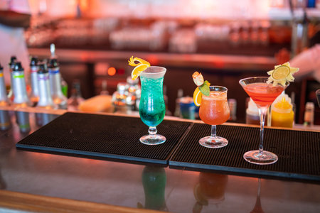 Exotic cocktails in glass glasses with straws and fruits and blurred bar accessories: shaker, spoon, spices Colorful cocktails on the bar counterの写真素材