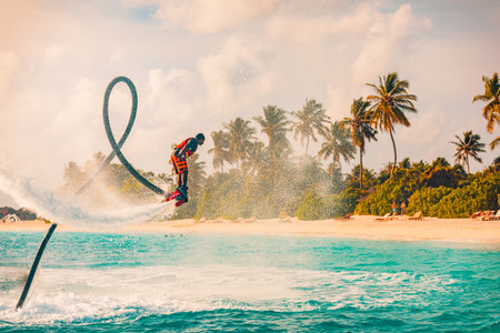 Maldives island sunset. Professional fly board rider doing back flip with tropical resort island background. Sunset sport and summer activity background, fun water sport 08.17.21のeditorial素材