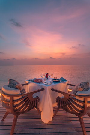 Amazing romantic anniversary honeymoon dinner. Beach on wooden deck candles under dream sunset sky. Romance and love couple luxury destination dinning, exotic table setup sea viewの写真素材
