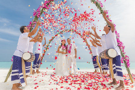 Asian wedding couple under weeding arch with flowers shower thrown around. Destination wedding, beach shore. Sunny happy moment. Exotic Maldivian beach wedding. 18.12.21. Maldivesのeditorial素材
