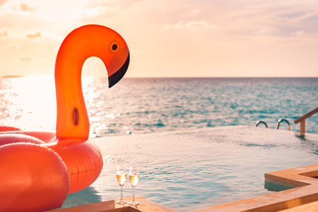 Luxury infinity swimming pool. Sunset holiday travel vacation background funny flamingo toy float header an champagne glasses as romantic couple, exotic love romance destinationの写真素材