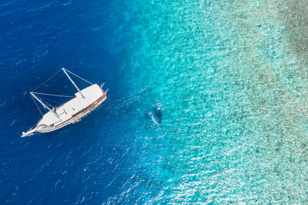 White sailboat, yacht in shallow tropical blue ocean coral sea reef. People snorkel whale shark....