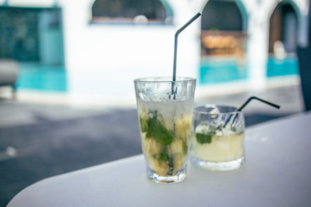 Mojito cocktail at the edge of a resort pool. Concept of luxury vacation. Outdoor bar pool background, relax vintage colored closeup. Relax pool with blurred hotelの写真素材