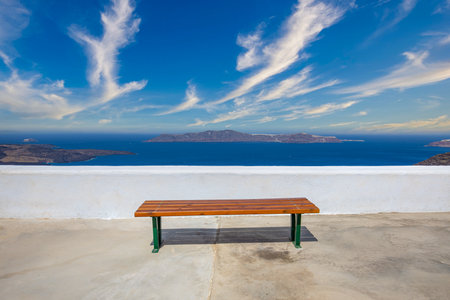 Wooden bench on terrace in Santorini island, Greece. Relaxing morning travel landscape, blue sea view, sunny cloudy sky. Idyllic vacation minimal backgroundの写真素材