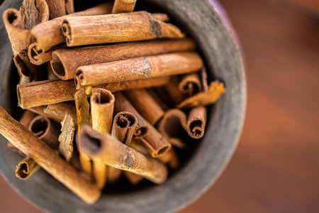Wooden bowl top view with cinnamon sticks on dark wooden background. Abstract food and cooking ingredients for dessert and healthy mealsの写真素材