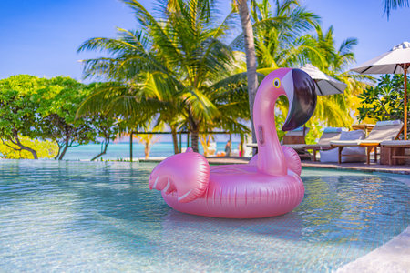 Summer fun tropical resort chairs, loungers umbrella under palm trees. Pink inflatable flamingo swimming pool water, summer beach panorama. Luxury lifestyle travel, summer vacationの写真素材