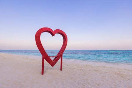 Valentine's Day background red heart shape. Wooden heart shape beach decoration. Sunset pastel colors clear sky sandy coast, seascape, horizon. Romantic honeymoon, romance and loveの写真素材