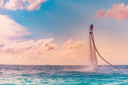 Maldives island sunset. Professional fly board rider doing back flip with tropical resort island background. Sunset sport and summer activity background, fun water sportの写真素材
