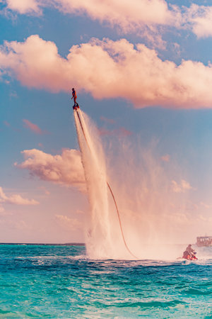 island sunset. Professional fly board rider doing back flip with tropical resort island background. Sunset sport and summer activity background, fun water sportの写真素材