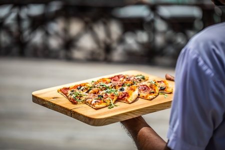 Sunny closeup outdoor restaurant waiter bring tasty Italian pizza to customers, hold wooden tray hands, serve guests. Mediterranean food artistic background, Mediterranean cuisineの写真素材