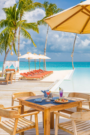 Luxury resort hotel poolside, outdoor restaurant beach, ocean sky, tropical island cafe, tables, food. Summer vacation  holiday, travel. Palm trees, infinity pool, cocktails, relaxの写真素材