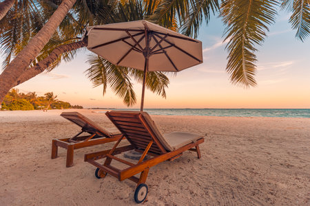 Beautiful tropical sunset couple two sun beds, loungers, umbrella under palm tree. White sand, sea view, romantic colorful twilight sky, calmness relaxation. Inspire beach resortの写真素材