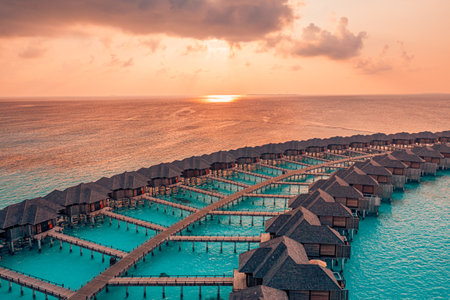 Aerial sunset landscape, luxury tropical resort water villas. Beautiful island beach orange sunrise sea sky. Amazing bird eyes view Maldives paradise bay. Exotic summer vacationの写真素材