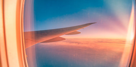 Amazing travel background with sunset sunrise sunlight seen from airplane window and wing, dreamy scene inspiring tourism and vacation vibes. Travel concept.の写真素材