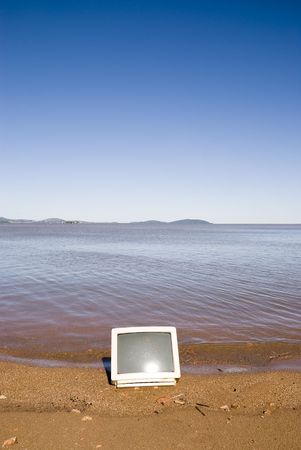 A computer monitor in the sand, with blue sky. Coastline shot.の写真素材