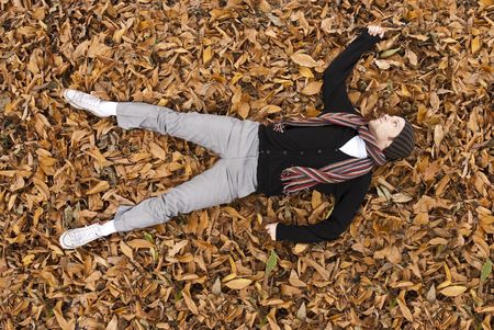 High angle full body shot of young man laying on the yellow leaves covered ground.の写真素材