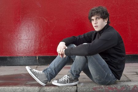Portrait of young man sitting against red backgroundの写真素材