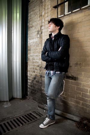 Full body street shot of young man leaning against brick wallの写真素材
