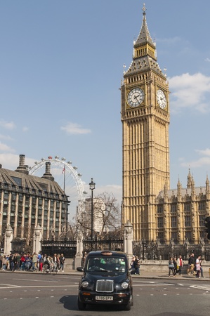 LONDON, UK - APRIL 02: Famous black cab driving by Houses of Parliament, with Big Ben prominent in...