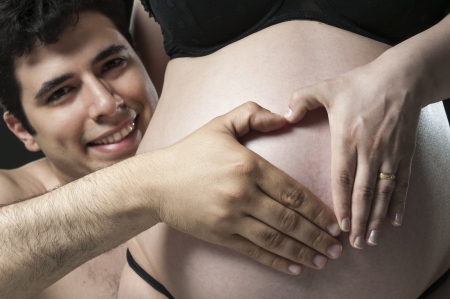 Portrait of young father making the shape of a heart on woman's baby belly and smiling.の写真素材