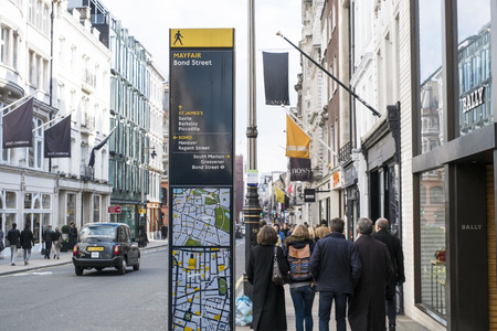 LONDON, UK - MARCH 14: Direction signs post in Mayfair, with famous shop banners and pedestrians passing by in the background. March 01, 2014 in London.のeditorial素材