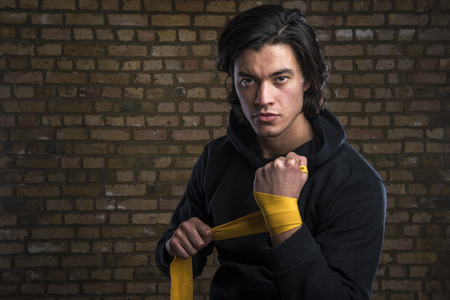 Young Malaysian boxer  wearing hoodie and wrapping straps around handsの写真素材