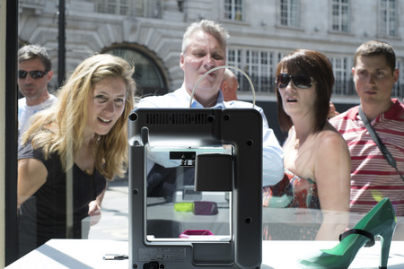LONDON, UK - MAY 31: Pedestrians intrigued with 3D printer in United Nude shop window. The shop,...