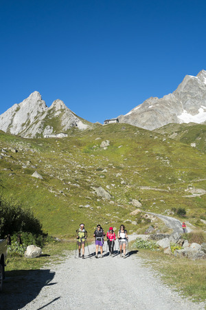 VAL VENY, ITALY - AUGUST 28: Hikers walking on dirt road with Elisabetta Soldini Refuge in the background. The refuge is on a stage of the popular Mont Blanc tour. August 28, 2014 in Val Veny.のeditorial素材