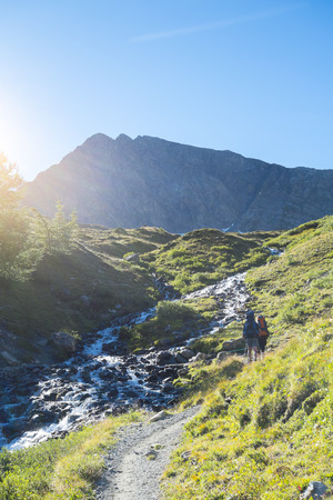 COMBAL, ITALY - AUGUST 28: Hikers walking up path by creek with Charmonts Peaks in the background. The area is on a stage of the popular European Mont Blanc tour. August 28, 2014 in Combal.のeditorial素材