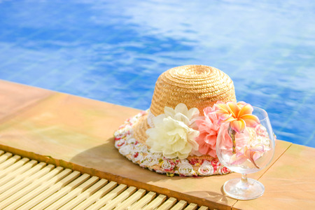 Flower inside glass and hat beside the poolの写真素材