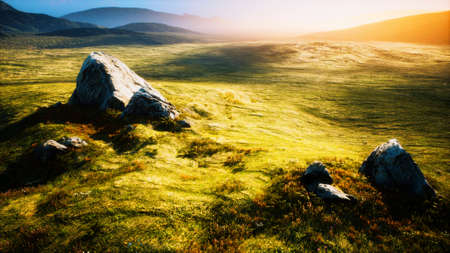 meadow with huge stones among the grass on the hillside at sunsetの写真素材