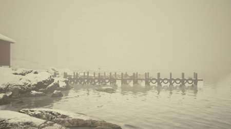 An old wooden pier covered in snow stands by a red building in the cold Norwegian sea.の写真素材