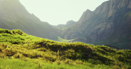 Rolling hills surrounded by majestic mountains show vibrant green grass illuminated by warm sunlight. The calmness of nature creates a peaceful and serene atmosphere.の写真素材