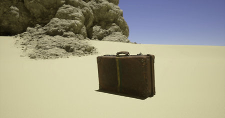 A weathered suitcase sits on a windswept sandy area next to rugged rock formations under a clear blue sky. The scene captures the isolation of a forgotten journey.の写真素材