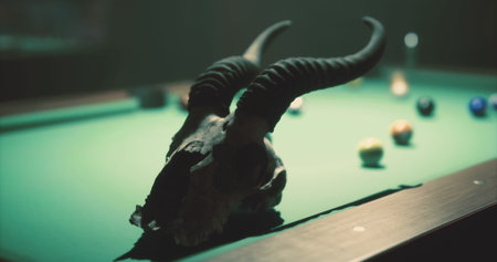 A ram skull rests on a green felt pool table, surrounded by colorful pool balls. The atmosphere is dim and moody, creating a mysterious setting for a game night.の写真素材