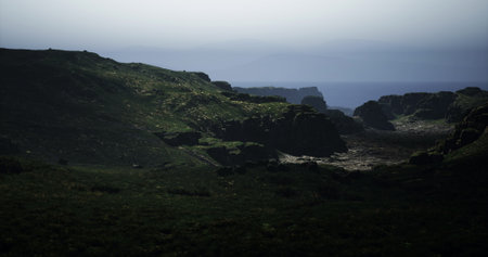 Rugged cliffs meet the vast ocean in a tranquil coastal landscape at dusk. The green pastures...