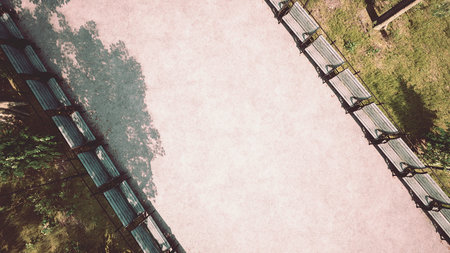 A winding pathway in a tranquil park is lined with benches, encouraging relaxation and reflection, bathed in dappled sunlight filtering through the trees overhead.の写真素材