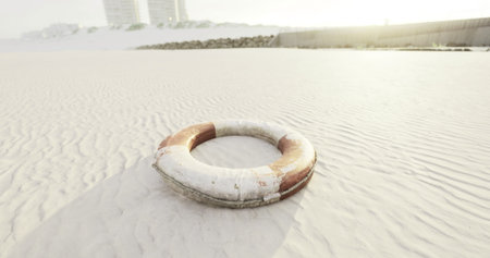 A lifebuoy sits abandoned on a sandy beach during sunrise, with soft light illuminating the...