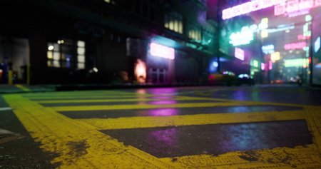 A vibrant urban street is bathed in neon lights reflecting off wet pavement at night. The atmosphere is lively with bright signs and city energy in the background.の写真素材