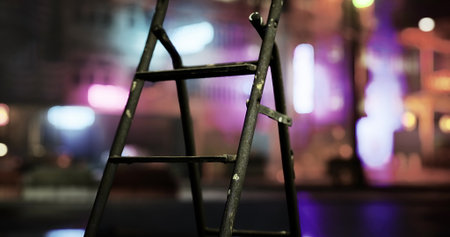 A ladder positioned in the foreground highlights an urban environment. Neon lights illuminate the background, creating a lively nightlife ambiance after sunset.の写真素材