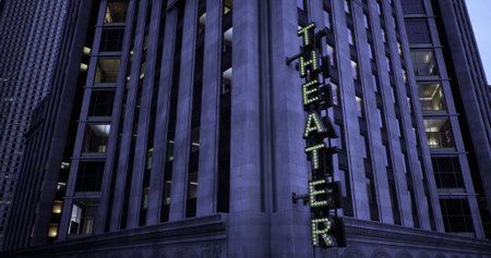 A historic theater building stands prominently in the city as the evening sky darkens. Neon lights spell out the word theater, attracting attention from passing pedestrians.の写真素材
