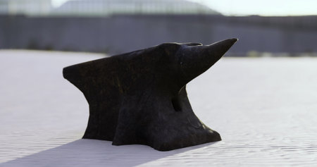 A solitary black anvil sits atop sun kissed sand, the waves gently lapping in the distance. The fantastic contrast of the dark metal against the light sandy texture creates a striking visual.の写真素材