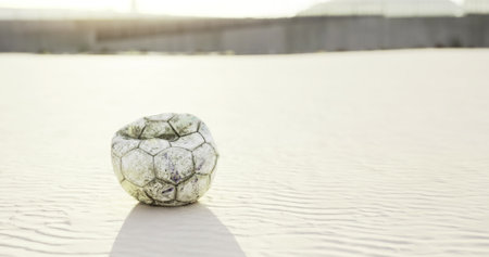 A worn soccer ball, partially buried in golden sand, glimmers under the warm sunlight. The coastline stretches in the background, casting an air of nostalgia and solitude.の写真素材