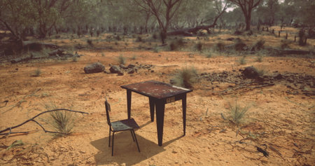 An old, weathered table stands alone in a barren landscape, accompanied by a single chair. Sparse vegetation surrounds them, showcasing the desolation of this arid environment.の写真素材