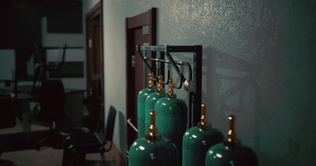 A row of green gas cylinders stands against a textured wall in a shadowy setting. Soft light highlights the bright valves, adding a touch of intrigue.の写真素材